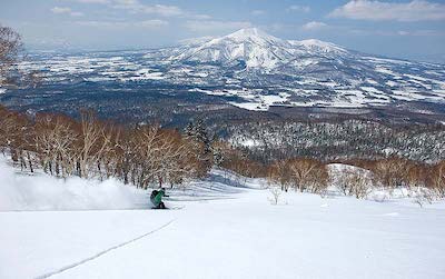 A skiers skiing down Mt Yohtei with Mt Niseko Annupuri forming a splendid backdrop